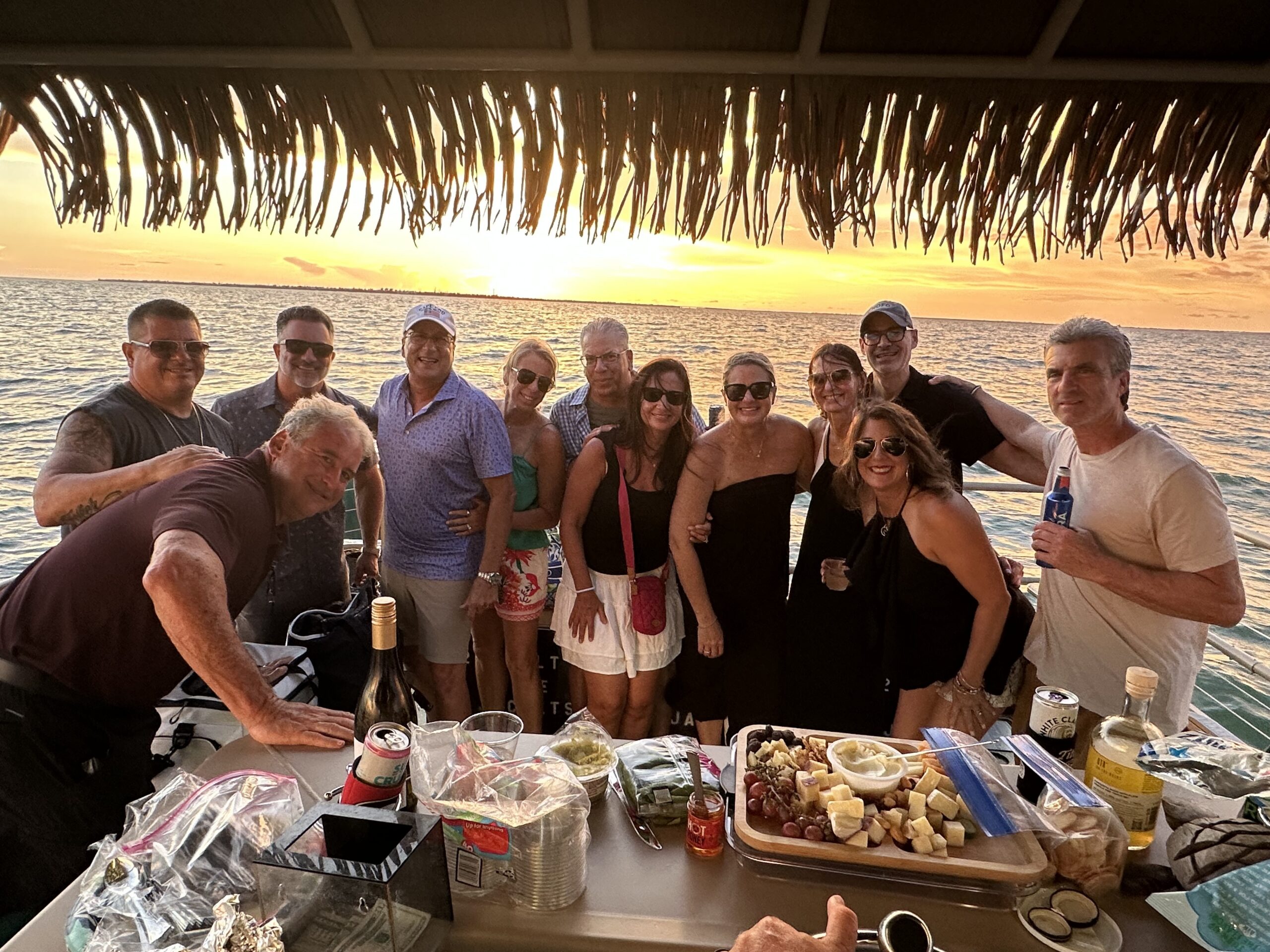 Friends celebrating aboard a tiki boat at sunset with food and drinks