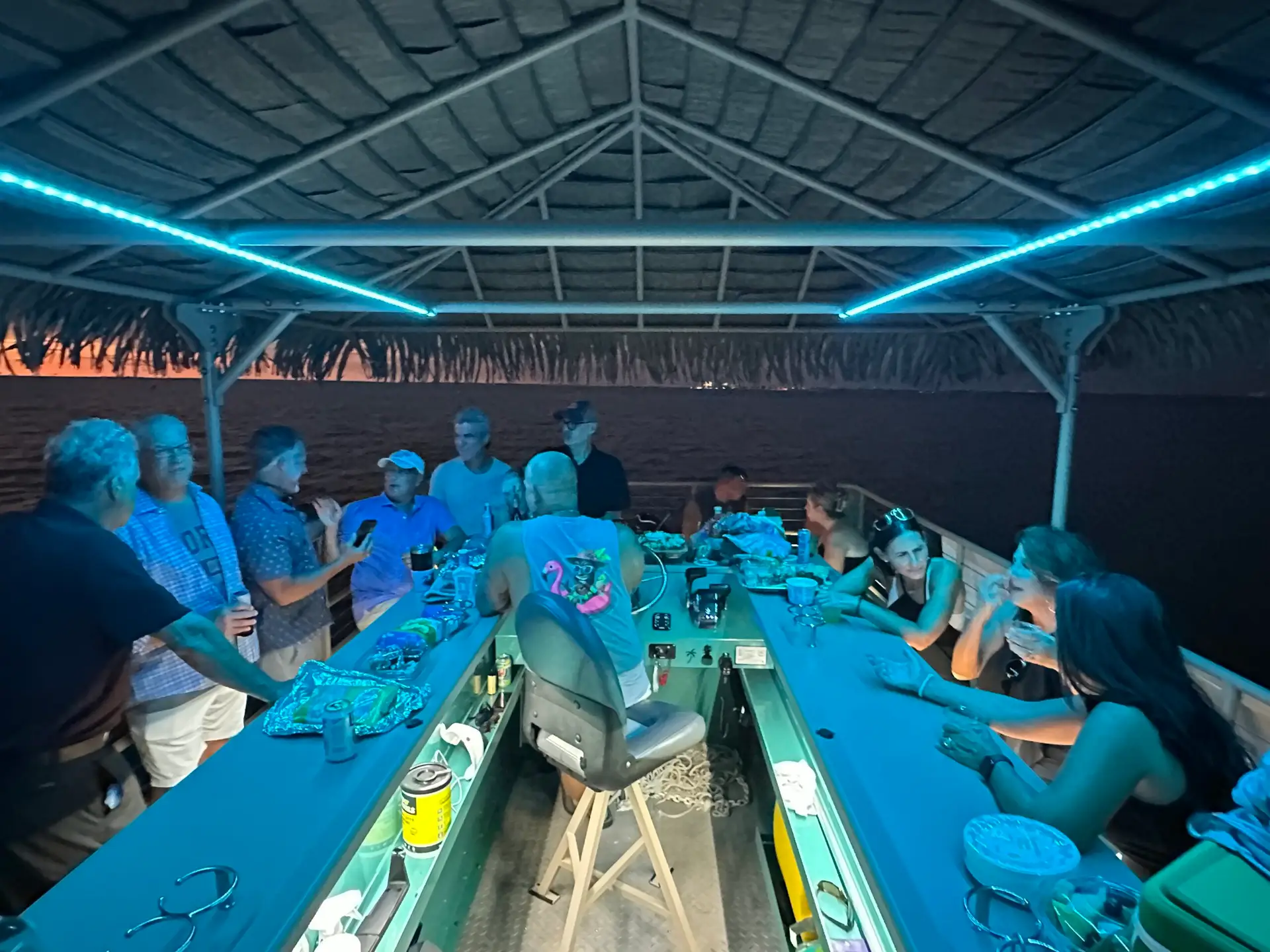 Guests celebrating aboard a tiki boat under blue evening lights